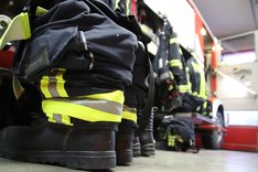 Mehrere Bekleidungsstücke von Feuerwehrpersonen hintereinander aufgereiht.